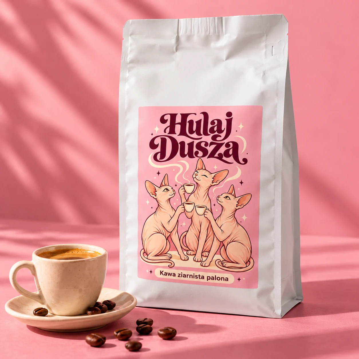 Wizualizacja kawy Hulaj Dusza: białe opakowanie z różową etykietą i trzema sfinksami obok filiżanki espresso